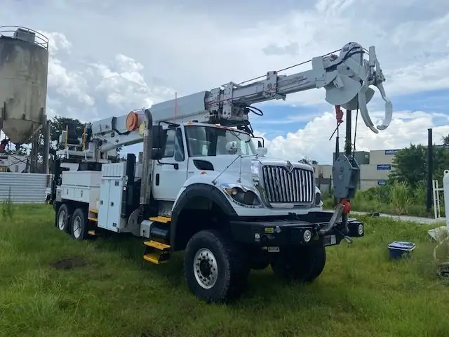 A white crane truck on its outriggers in a grass lot