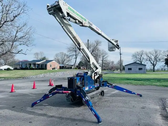 A blue tracked spider lift on spread outriggers inside a ring of orange cones